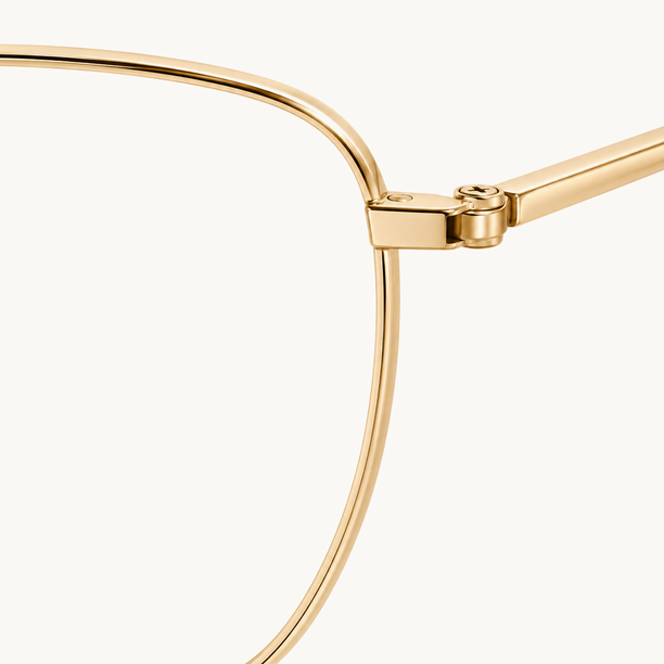 Gọng kính kim loại mảnh màu vàng gold chụp cận cảnh, thấy rõ bản lề, con vít nhỏ và càng kính.
